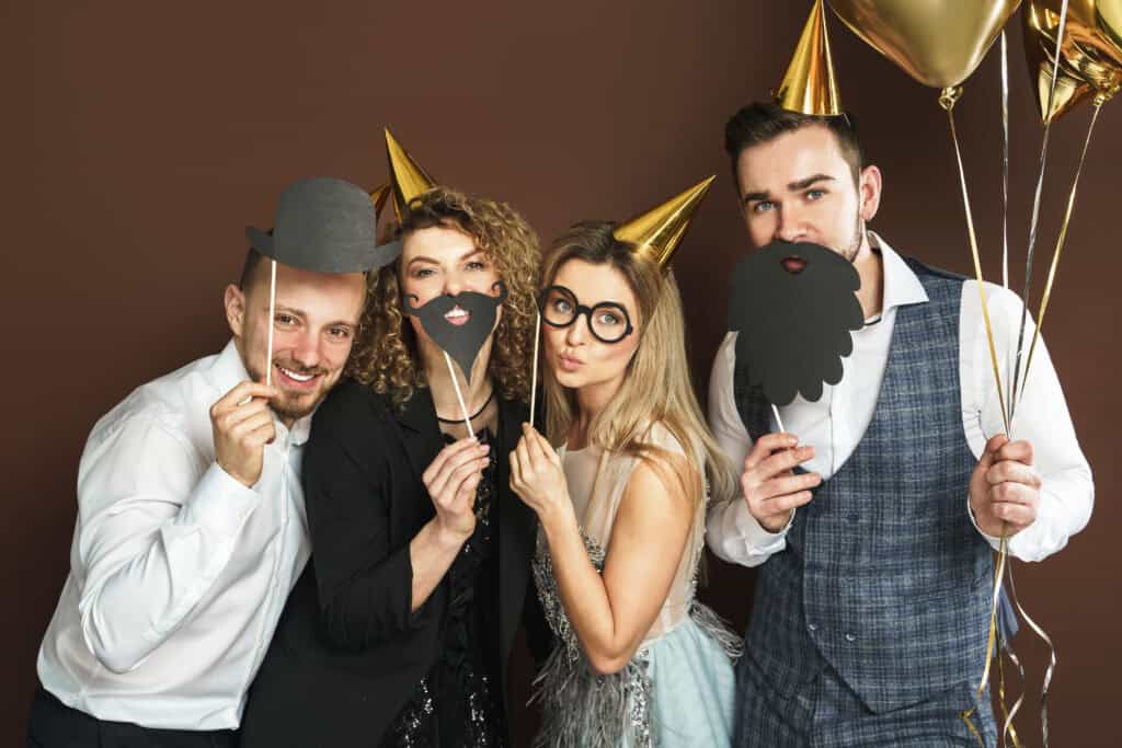 Group of people posing with photo booth props and party hats.