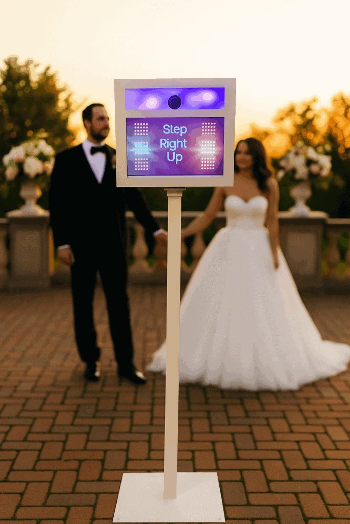 A sleek, open-air photo booth with a 'Step Right Up' sign and a bride and groom in the background.